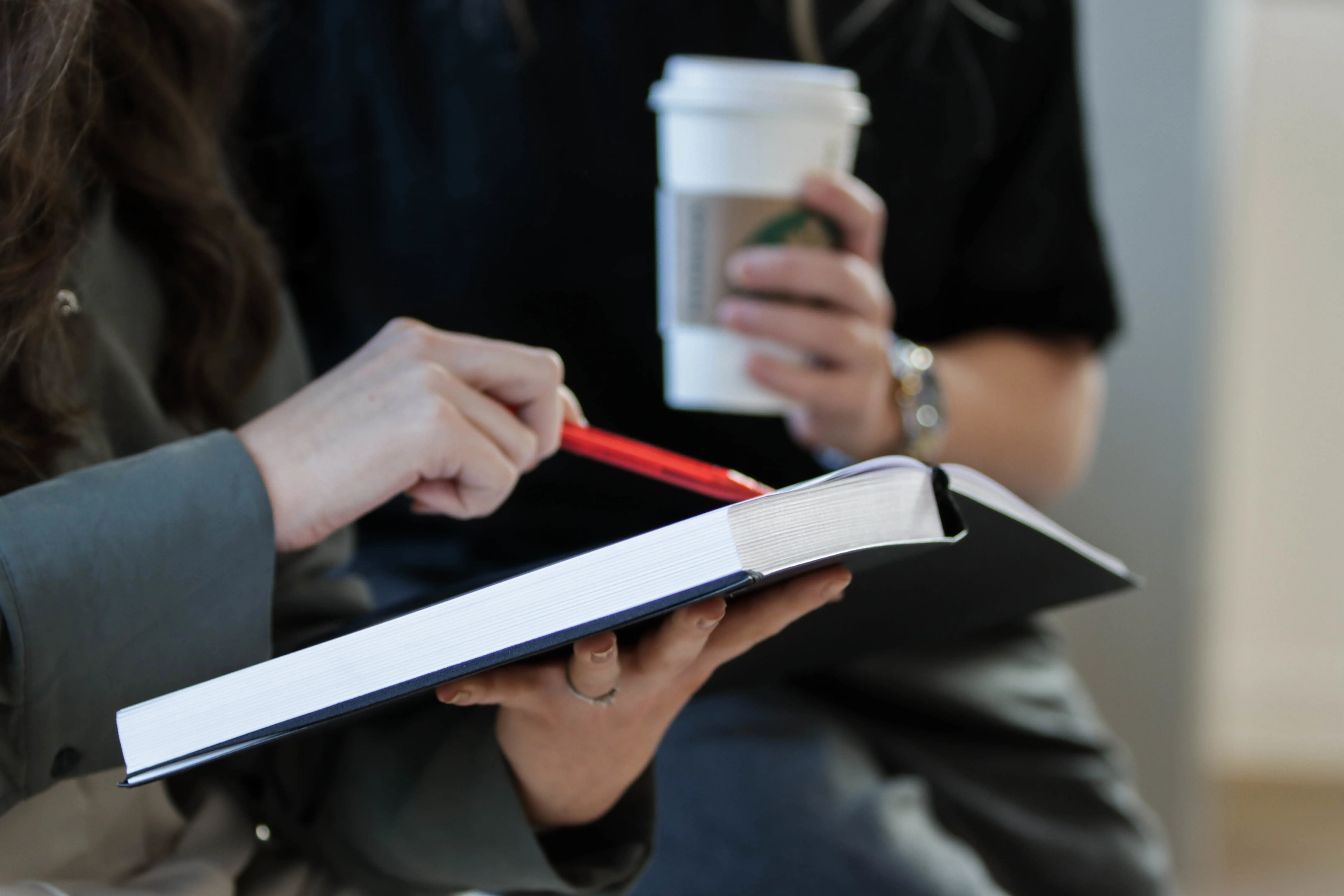 Close-up of hands holding a book and a takeaway coffee cup