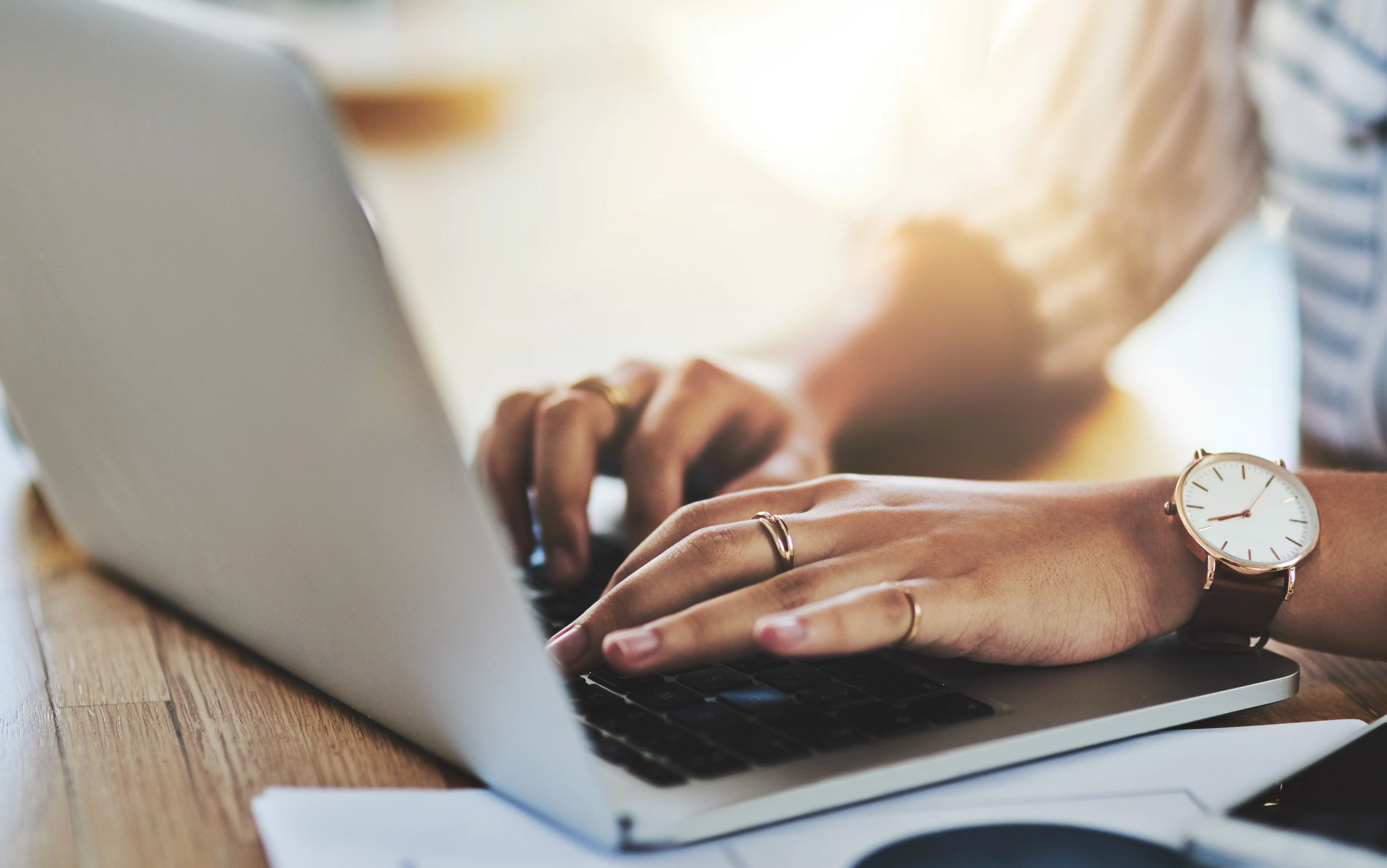 Woman working Woman's hands typing on a laptop keyboard, wearing rings and a wristwatch.