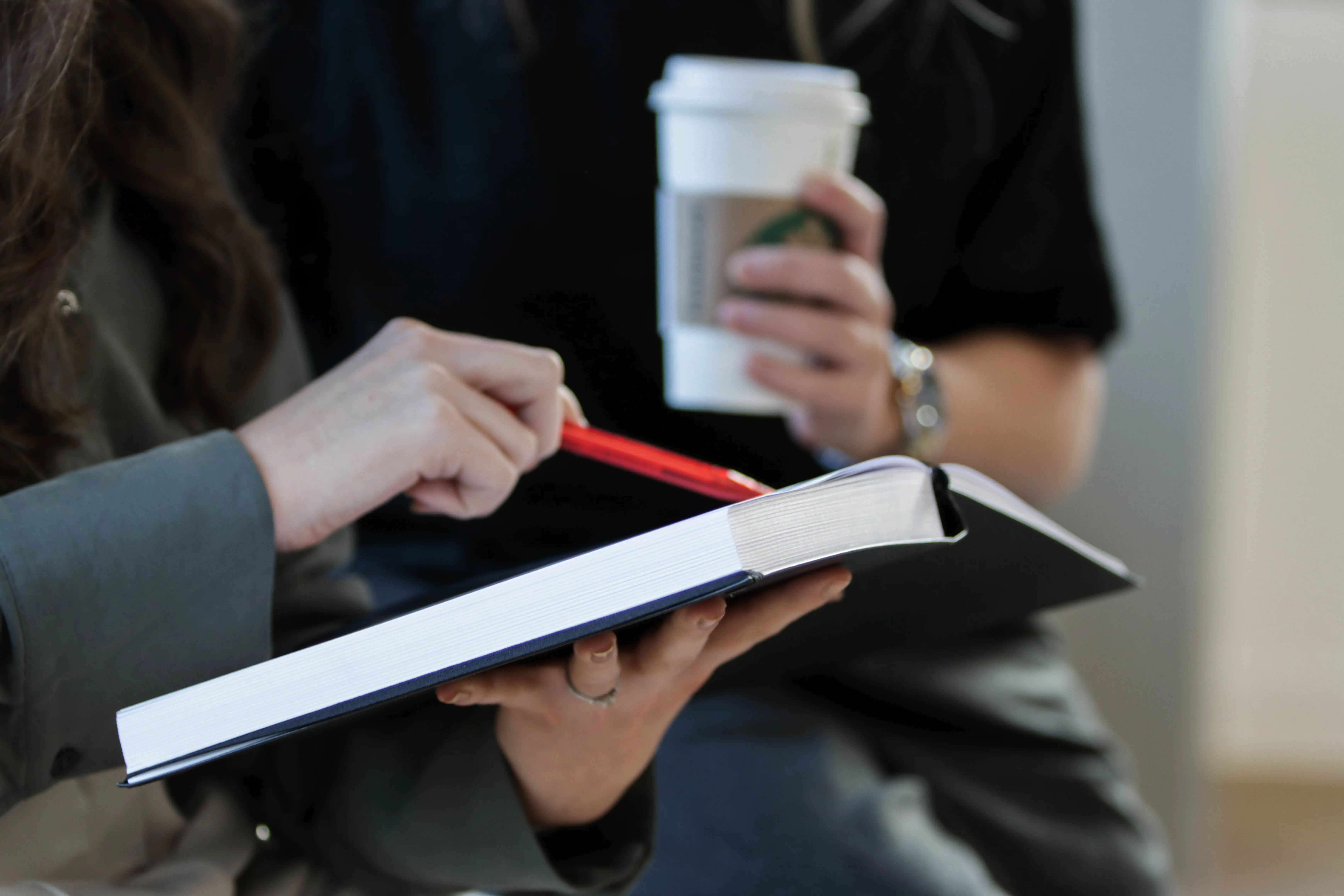 Close-up of hands holding a coffee cup and pointing at an open notebook during a meeting