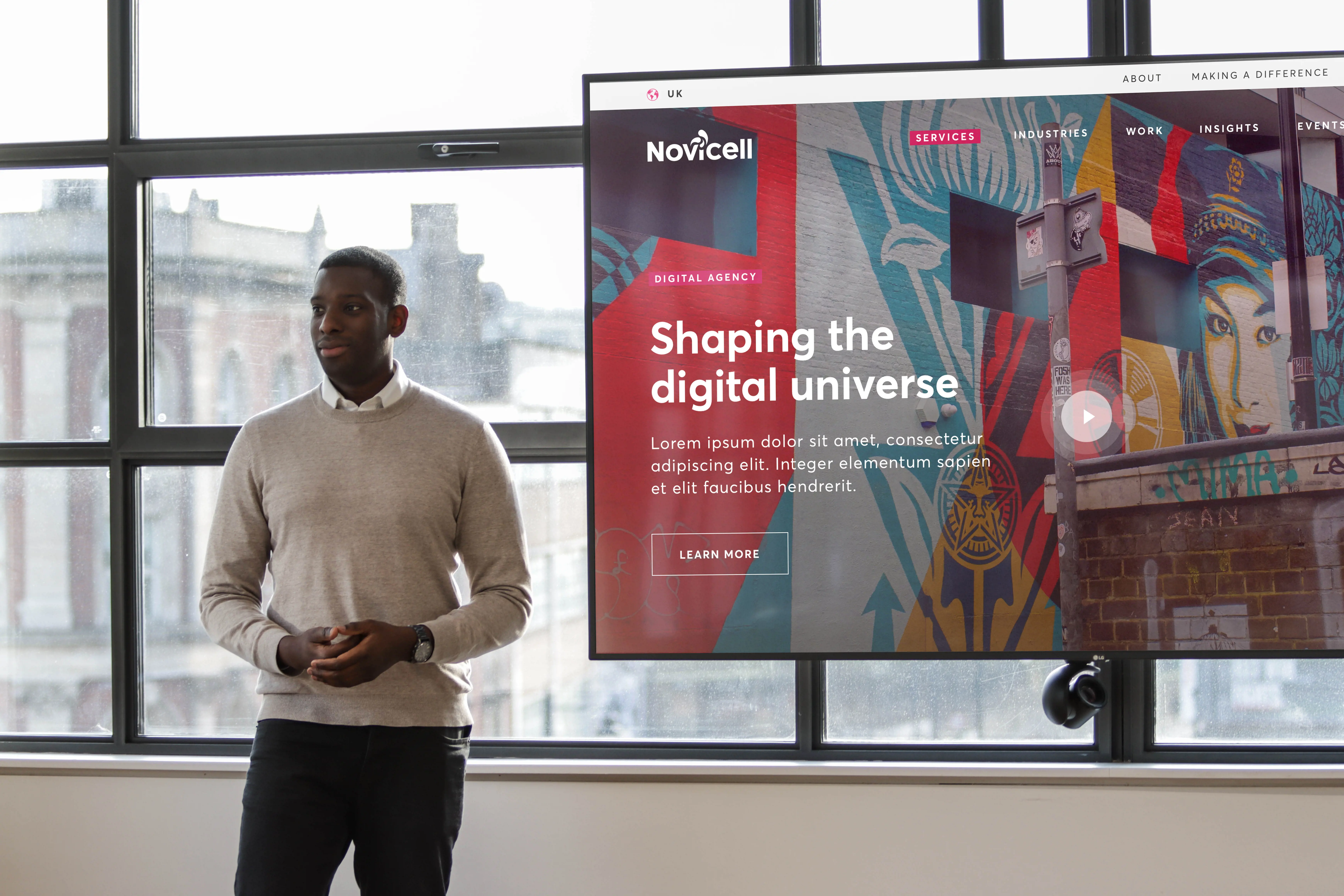 A man in business casual attire standing next to a large screen displaying a Novicell website