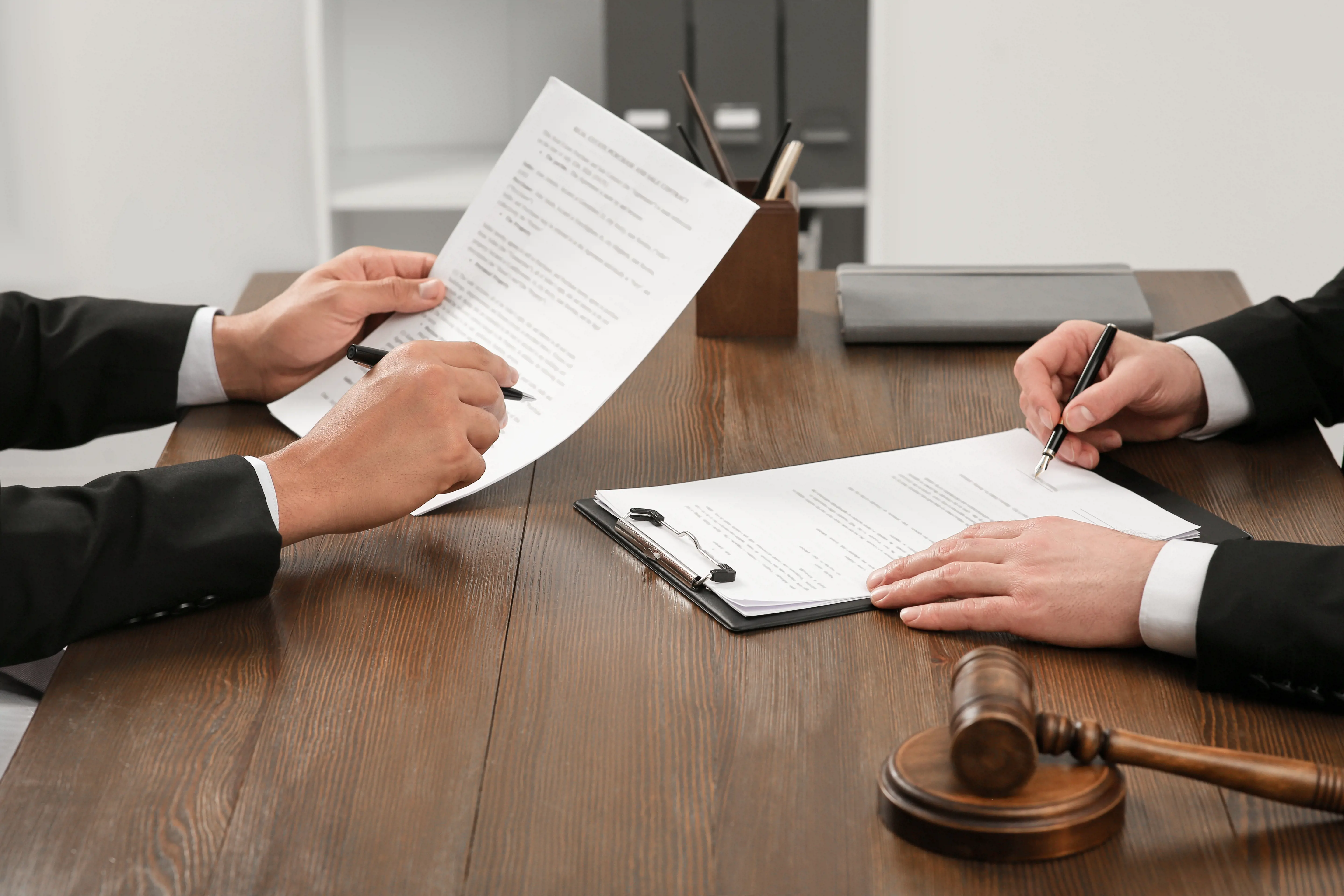 Two lawyers in suits reviewing and signing legal documents at a wooden desk