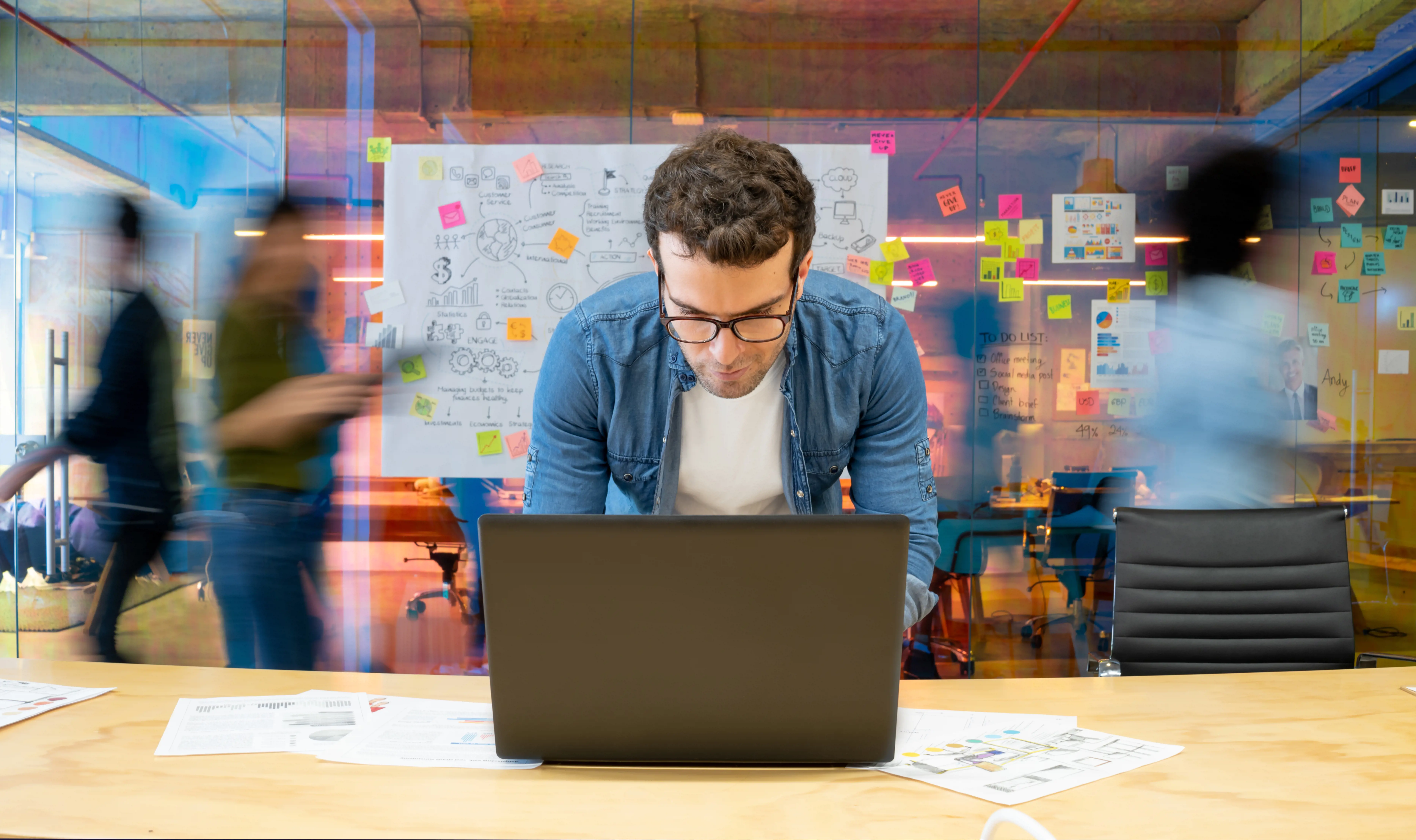 man working on laptop in front of wall of post its