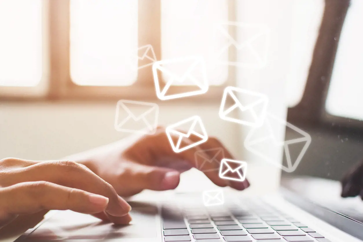 Email Marketing Concept Hands typing on a laptop keyboard with glowing envelope icons floating above, representing email communication.