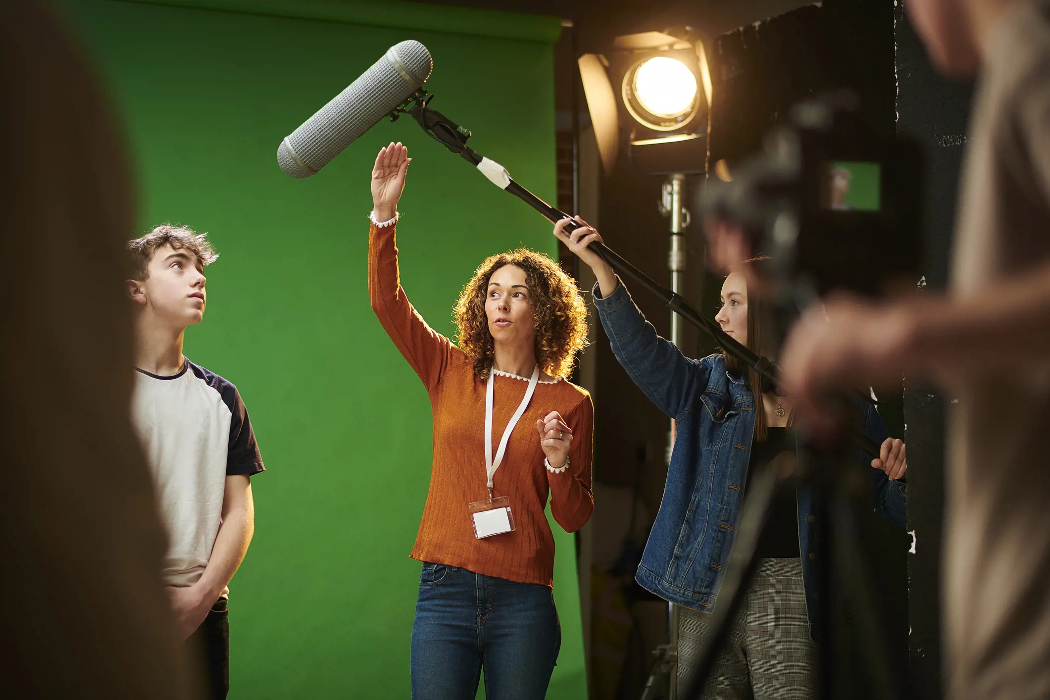 Film crew working on a green screen set with lighting equipment and a boom microphone